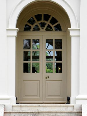 Front view of a classic white building entrance with arched doorway and columns, featuring glass windows and metal railings.